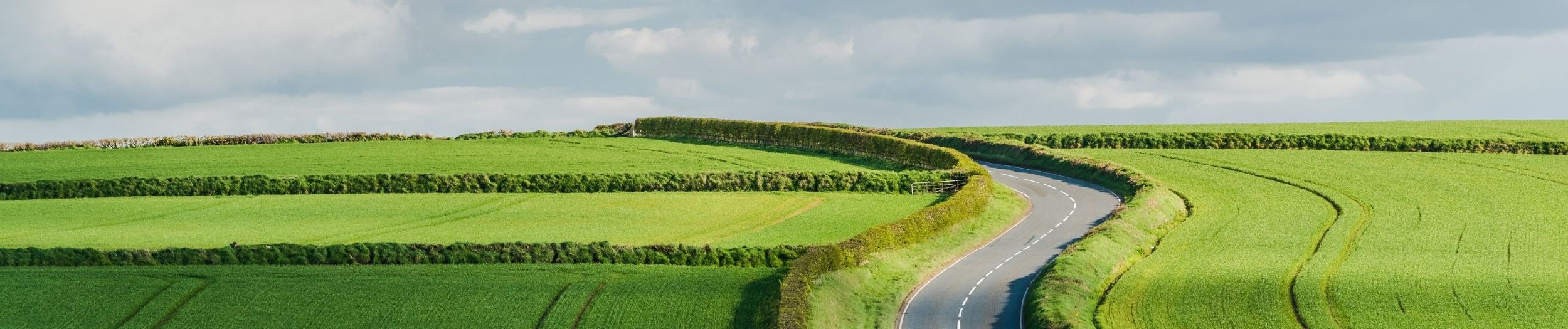 Rural road on rolling hills in countryside, with lonely driving car