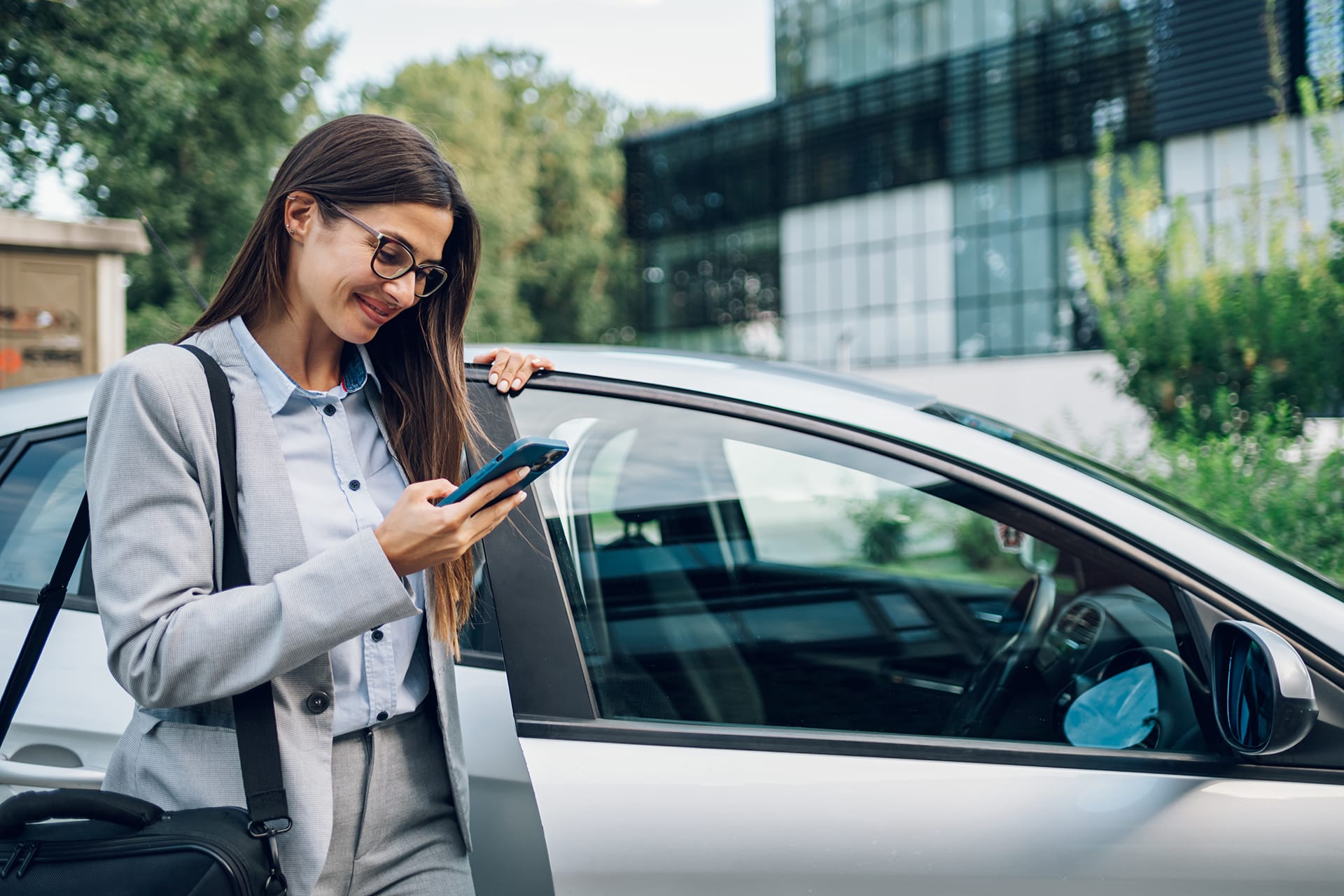 Business woman looking on her phone before getting in a car